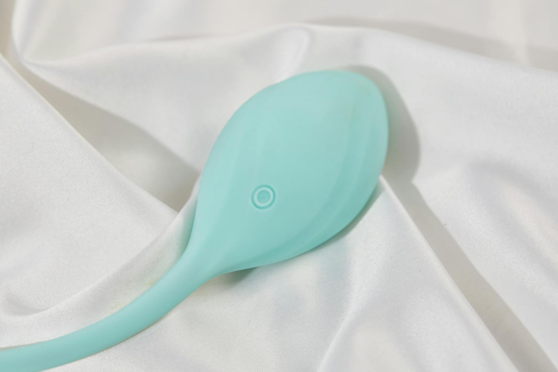 A teal silicone vibrator on smooth white silk, representing couples pleasure without pressure