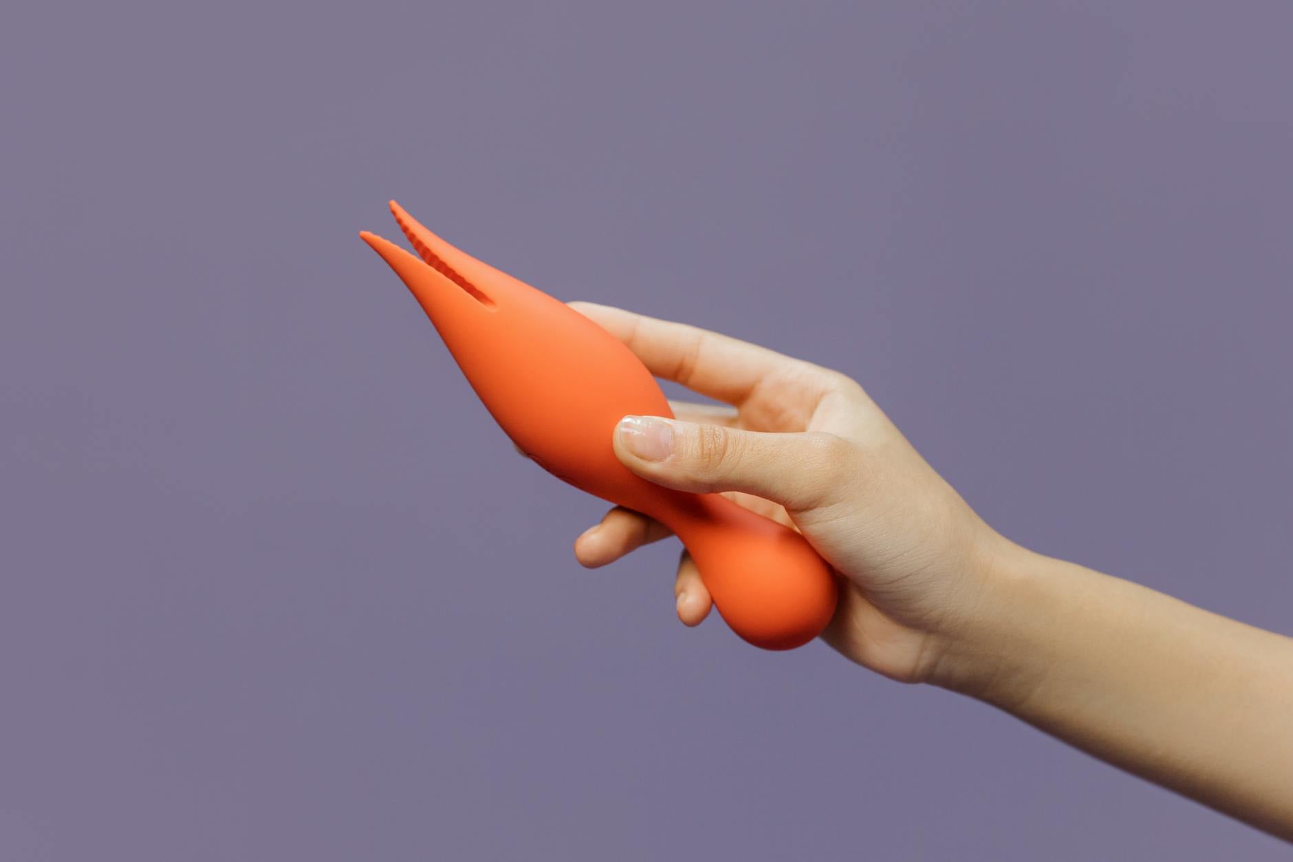 A hand holding a sleek modern clitoral vibrator against a minimalist purple backdrop, symbolizing confidence in pleasure and communication.