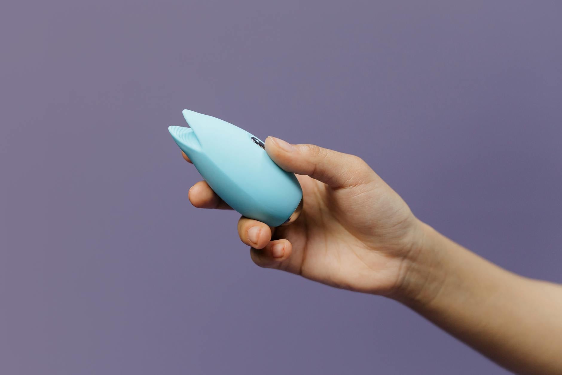 A person holds a silicone sex toy against a purple background, exploring self-pleasure and intimate wellness