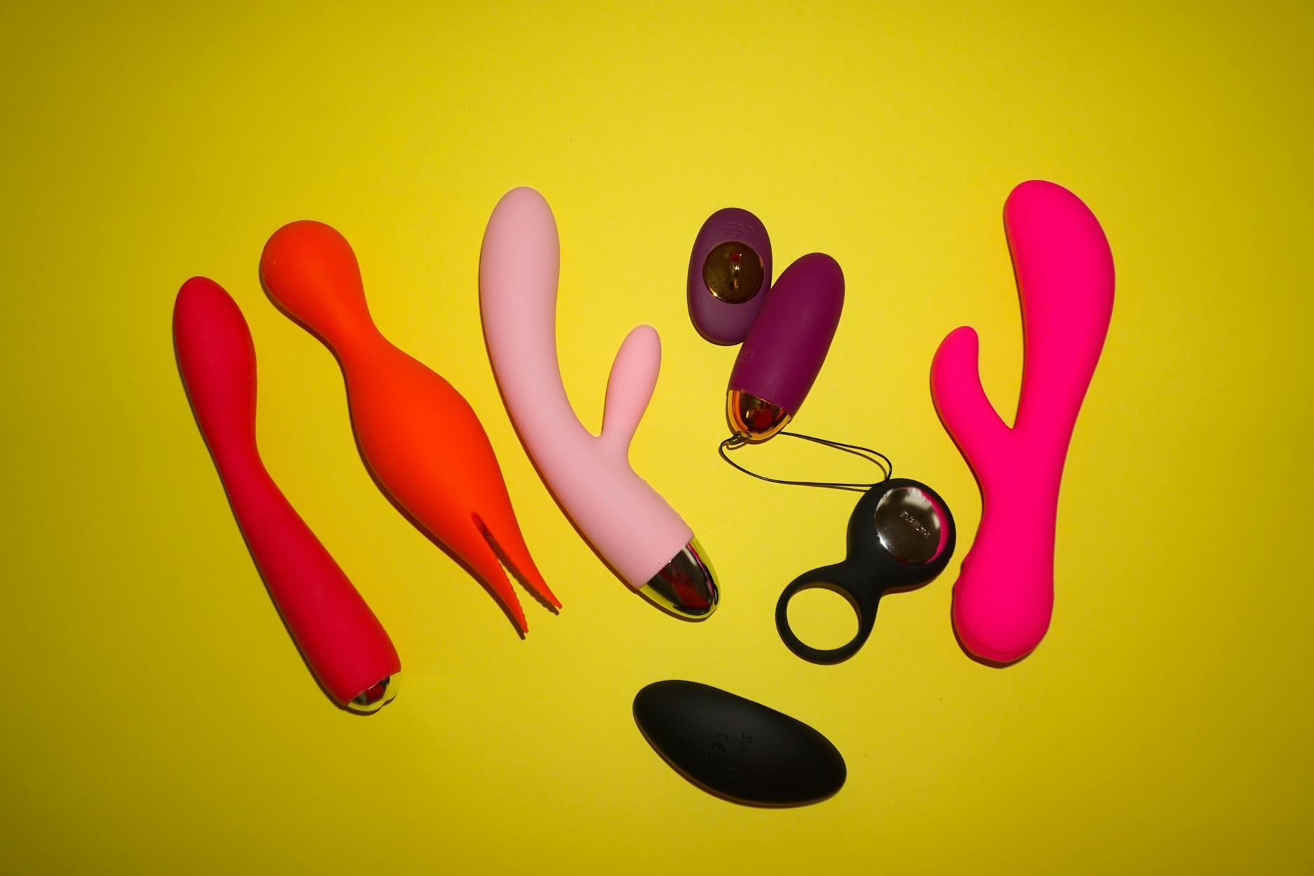 Colorful clitoral vibrators arranged on bright yellow background, showcasing modern pleasure toys